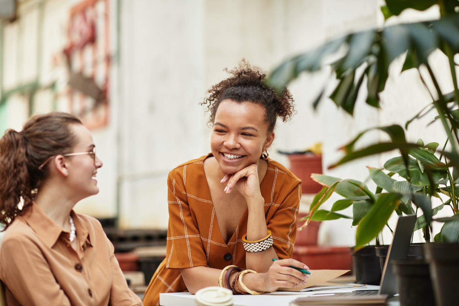 Two colleagues talking and laughing together over a laptop in a bright office
