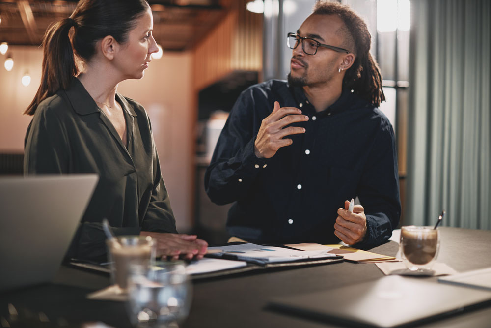 A senior colleague talking through a piece of work with a junior at a table of papers