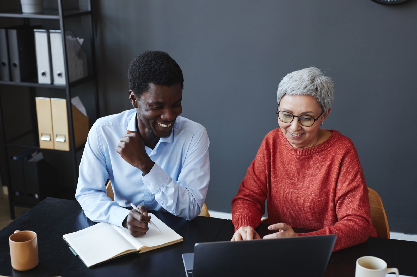 A senior colleague and a junior working through something together at a laptop