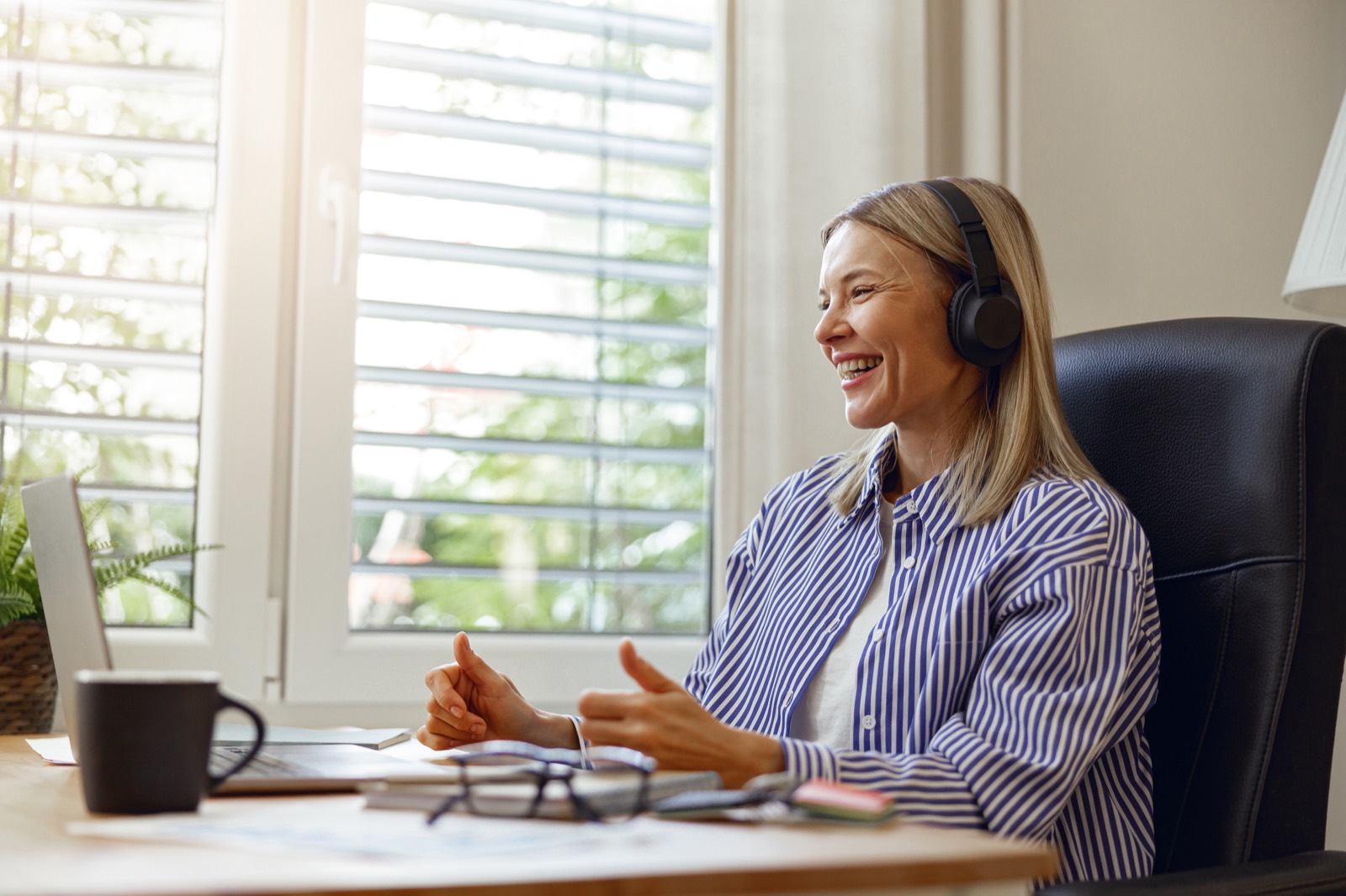 A manager on headphones smiling during a remote meeting at her desk